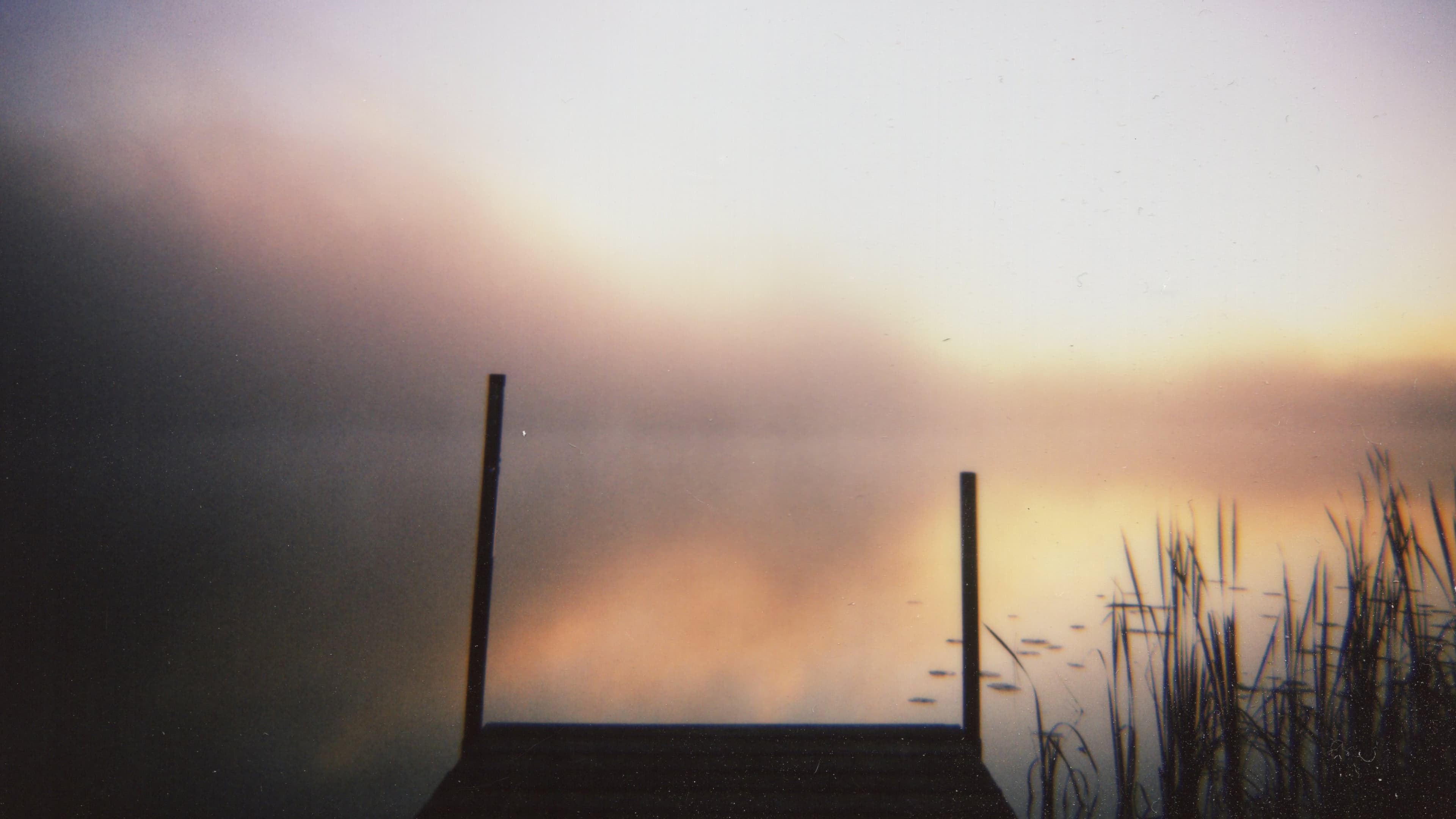 a wood deck in the foreground of a still lake at dawn
